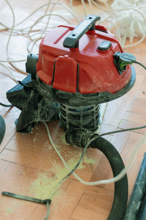 A close-up shot shows a red shop vacuum cleaner amidst drywall dust and tools during a home...