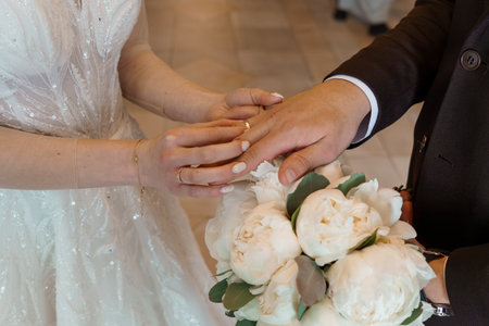 Romantic wedding moment capturing a close-up view of a groom placing a gold wedding ring on the bride's finger, adorned in a sparkling dress, bouquet. symbolizes loveの写真素材