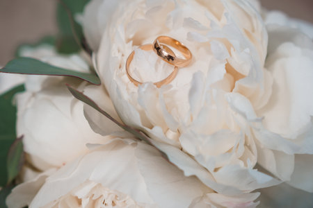 Golden wedding rings resting upon a lush white peony bouquet represent enduring love, bridal celebrations, and the precious symbolism of commitment and lifelong partnershipの写真素材