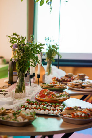 An elegant buffet table is set with colorful crostini, caprese skewers, and wildflower arrangements,...