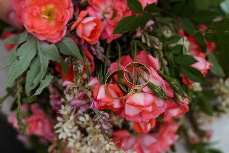 Romantic close-up shot of golden wedding rings nestled within a lush arrangement of coral-colored roses, ideal for conveying love, marriage, and commitmentの写真素材