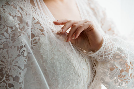 Intimate wedding detail showing a bride's delicate hand gently caressing the intricate lace of her flowing ivory gown, capturing romanceの写真素材