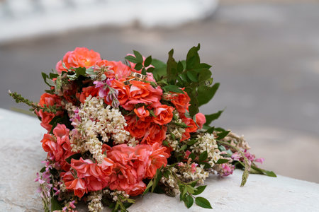 A vibrant wedding bouquet composed of coral peach roses and delicate white baby's breath encircles...