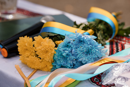A vibrant bouquet featuring yellow and blue chrysanthemums with ribbons rests on a table decorated...