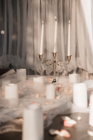 Serene image of a silver candelabra with lit white taper candles surrounded by pillar candles and rose petals on a table draped with sheer fabrics, creating a romantic moodの写真素材