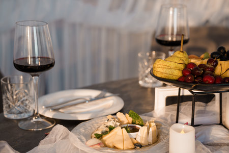 Intimate scene showcasing red wine glasses, a cheese platter with fruit, and candlelight on a dark wood table, evoking romance, relaxation, and fine diningの写真素材