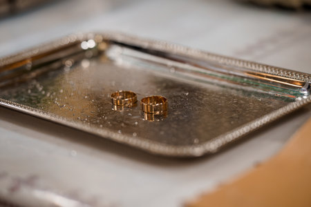 Close-up view of two gold wedding bands resting on a beautifully decorated silver tray, representing an intimate moment during a marriage ceremonyの写真素材