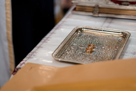 Close-up of golden wedding rings placed on a silver tray sprinkled with shiny crystals, resting on a...