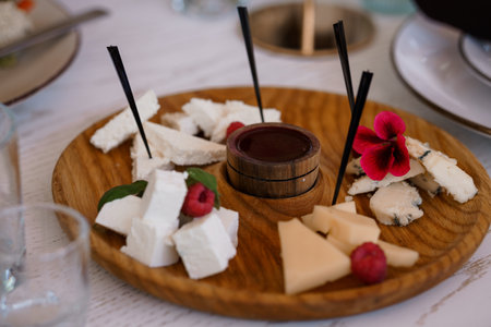 A beautifully arranged cheese board features varied cheeses and fresh raspberries, adorned with vibrant red flowers, centered around a dark dip, ideal for social gatheringsの写真素材