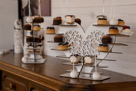 Beautiful wedding confection arrangement featuring a heart-shaped cake pop stand with chocolate and vanilla treats, presented on a warm wooden table, perfect for event planningの写真素材
