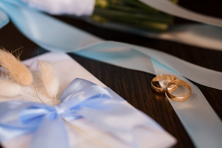 A close-up shot showcases golden wedding rings nestled amongst soft blue ribbons and sprigs of delicate flowers, symbolizing love and commitment, perfect for wedding announcementsの写真素材
