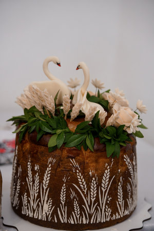 A beautifully decorated wedding cake features a two-swan motif, ivory flowers, and a rustic bark-like texture adorned with wheat.の写真素材