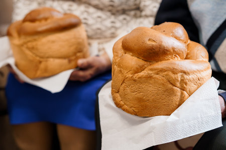 Two soft, golden brown Japanese milk bread loaves are carefully held in hands, wrapped in white paper, showing a rustic texture. a bakery scene, food photographyの写真素材