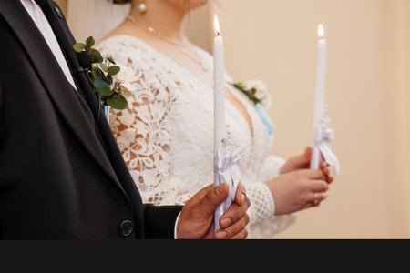 A heartwarming wedding scene showcasing a bride in a delicate lace gown and groom in a classic black suit holding lit unity candles during their ceremony, symbolizing eternal loveの写真素材