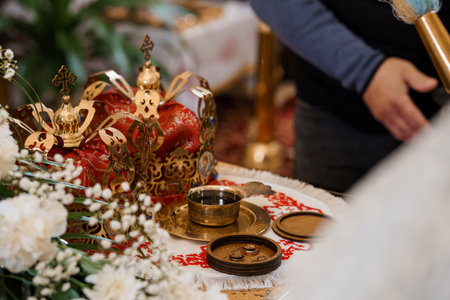 A close-up view of an Orthodox Christian wedding ceremony featuring golden crowns, wedding rings, a silver chalice, and red embroidered cloth, symbolizing unionの写真素材