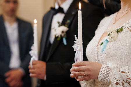 Beautiful shot of an Orthodox wedding ceremony with the bride and groom lighting candles, symbolizing unity and faith. elegant lace dress and dark suit detailの写真素材