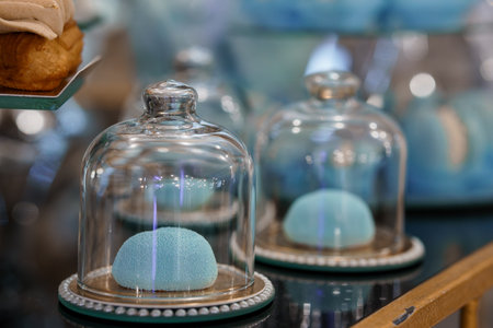 This shot showcases delicate pastel blue macarons presented under clear glass cloches within a charming bakery setting, highlighting a vintage aesthetic with selective focus on the dessertsの写真素材