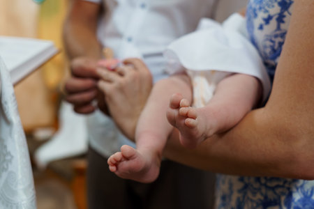 A close-up image captures delicate baby feet held during a christening ceremony, symbolizing new life, faith, and family connection. a blue floral dress is visibleの写真素材