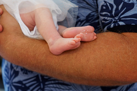 A heartwarming close-up showcasing a father lovingly holding his newborn baby's delicate feet, blue floral shirt visible, conveying familial affection and joyの写真素材
