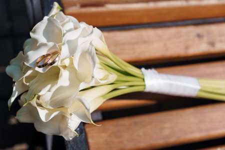 A beautiful, intimate shot featuring golden wedding rings resting on a pristine white calla lily bouquet symbolizing love, commitment and celebration, ideal for wedding-themed contentの写真素材