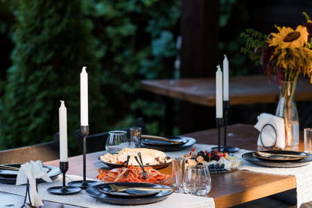 Elegant outdoor dinner with charcuterie spread, black tableware, tall candles, and a sunflower...