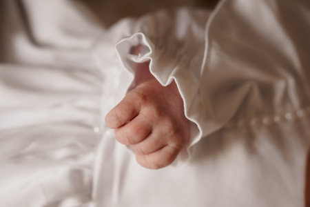 A tender close-up shows a newborn babys hand tightly gripping their mothers white shirt, symbolizing...
