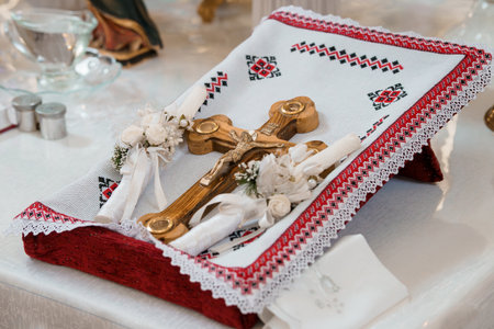 A close-up shot of an Orthodox Christian baptism ritual featuring a wooden cross, delicate white flowers, and an embroidered linen cloth, symbolizing faith and new beginningsの写真素材