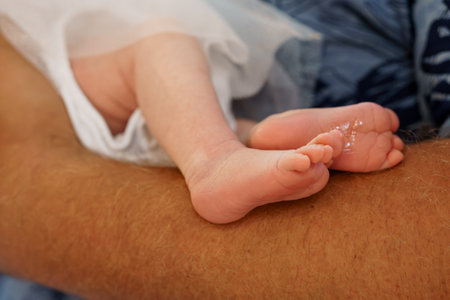 A heartwarming close-up showcases a newborn baby's delicate feet gently resting upon a father's...