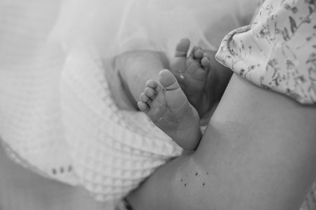 Tender black and white close-up of a newborn baby's feet resting on a mother's lap. symbolizes new...