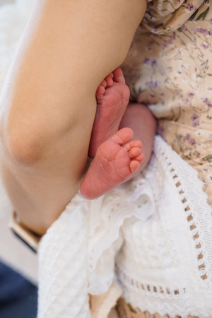 A mother lovingly cradles her newborn baby's tiny feet, showcasing a tender moment of parental connection with a soft floral dress as the backdropの写真素材