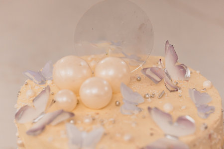 A beautifully decorated peach-colored cake adorned with white pearl candies, delicate lavender sugar shards and a transparent isomalt sail, perfect for wedding dessertsの写真素材