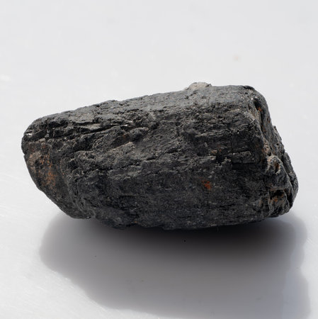 Polished black tourmaline rock on a white background, showing a rough mineral specimen often used...