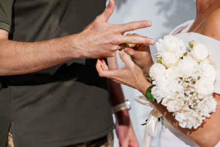 Romantic Wedding Ring Exchange Ceremony with White Bouquet, Green Suit, Blurred Background, Soft Light, Intimate Moment.の写真素材