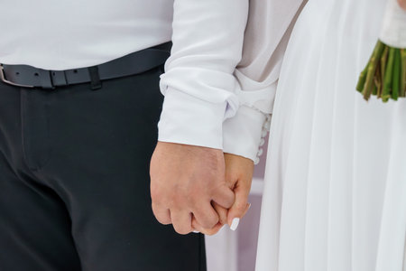 Wedding Day Hands Holding. Groom in Black Suit, Brides White Dress, Close-Up View. Symbolic Love, Commitment, Bouquet, Elegant Styleの写真素材