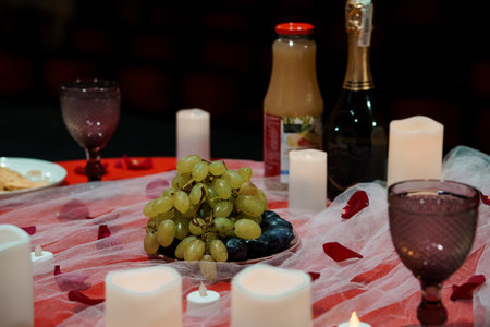 A dimly lit romantic dinner scene features two wine glasses, juice, a bottle of sparkling wine,...
