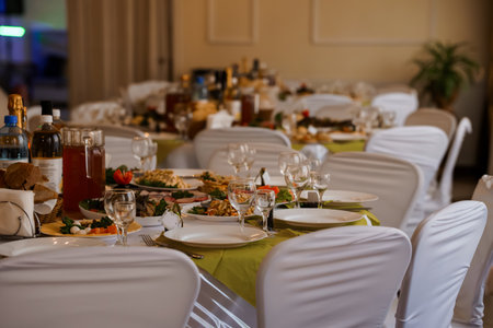 Elegant Banquet Table Setting with Wine, Fine Dining Food, and White Chairs in a Dimly Lit Event Venue.の写真素材