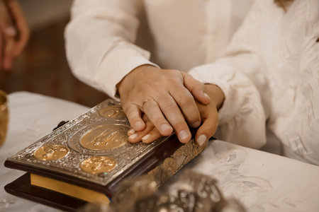 Intimate view of hands holding a gilded religious book during an Orthodox wedding, showcasing golden...