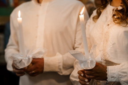 A close-up of a bride and groom holding burning candles during an Orthodox Christian wedding ceremony, symbolizing unity, faith, and tradition in a church settingの写真素材
