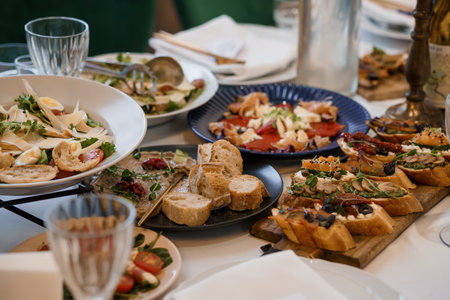 Appetizing Antipasto Table Spread Featuring Bruschetta, Salads, and Olives, Rustic Italian Cuisine, Dark Blue Plates, and White Linen.の写真素材