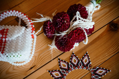 A richly detailed close-up showcasing elegant wedding accessories deep burgundy dahlias, lustrous pearl strands, a delicate beaded purse, and a striking crown arranged on a warm wooden surface, evoking a vintage, romantic moodの写真素材