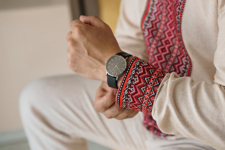 Close-up of a man wearing a classic black wristwatch and a beautifully detailed traditional...