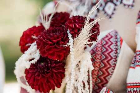 A detailed close-up captures a richly decorated Ukrainian wedding garland featuring vibrant red dahlias interwoven with delicate beaded necklaces and ornate embroidered clothingの写真素材