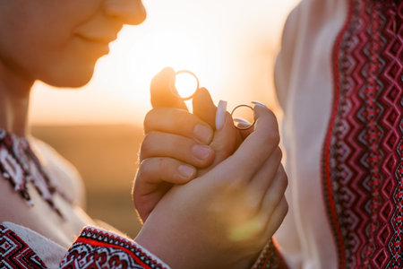 A close-up of a couple exchanging wedding rings during a golden hour sunset ceremony, showing traditional Ukrainian embroidered clothing. a symbol of love and commitmentの写真素材