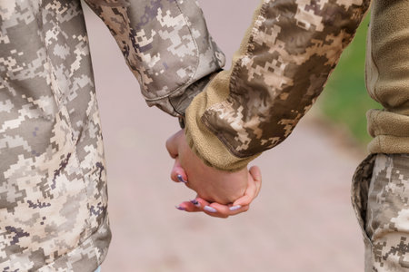 Two US Army soldiers in digital camouflage uniforms tenderly hold hands outdoors, conveying support and connection. a powerful image representing camaraderie, love, and military relationshipsの写真素材