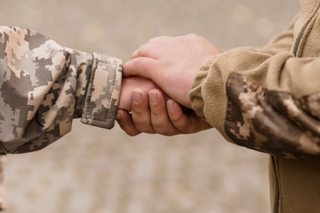Two soldiers clasp hands demonstrating camaraderie, support, and trust within a military context. the image conveys a sense of unity and shared purpose in a dusty environmentの写真素材
