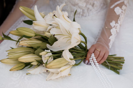 A close-up shot showcases a bride holding a beautiful bouquet of white lilies, symbolizing purity and love, with a delicate lace wedding dress visible. perfect for wedding-themed designsの写真素材
