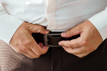 Groom Fastening Brown Leather Belt with Black Buckle, Wedding Preparation, Close-Up of Mans Hands,...