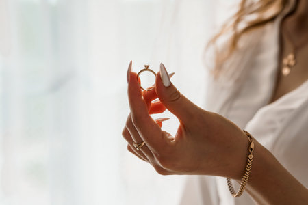 Golden Engagement Ring Displayed by a Womans Hand, Soft Focus, Wedding Jewelry, Diamond, Luxury, Indoor, White Fabric, Feminine Style.の写真素材