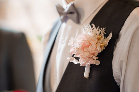 A close-up of a groom's chest showing a sophisticated black vest, white dress shirt, gray bow tie,...