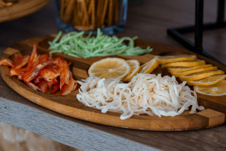 A rustic wooden platter features vibrant lemon slices, shredded zucchini, and crispy bacon strips,...